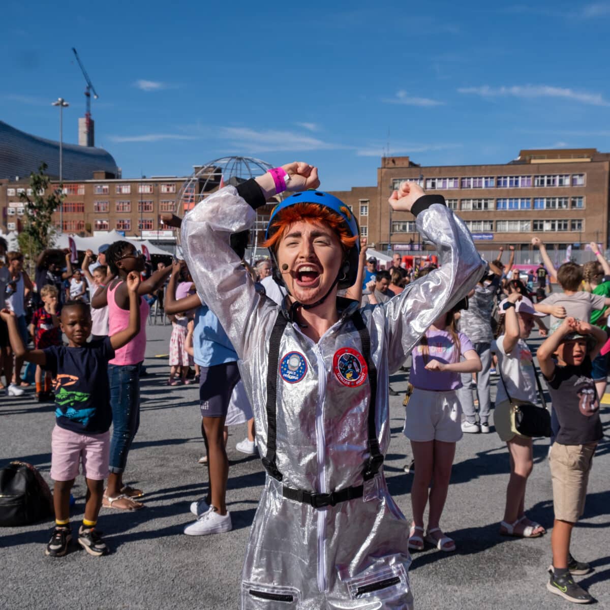 A performer dressed in an astronaut costume dances in the middle of a crowd.