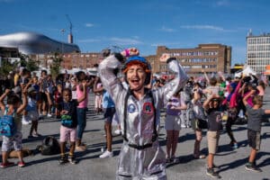 A performer dressed in an astronaut costume dances in the middle of a crowd.