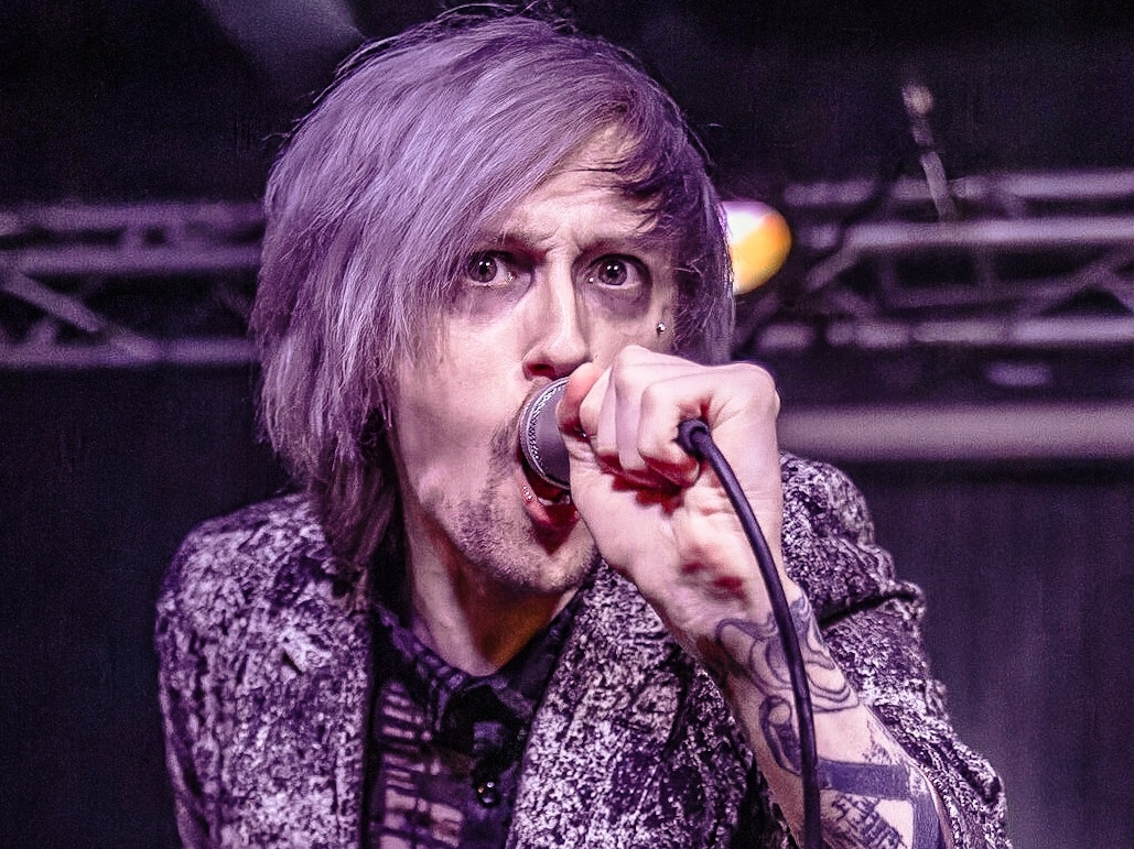 Performer with purple hair and clothing sings into the mic.