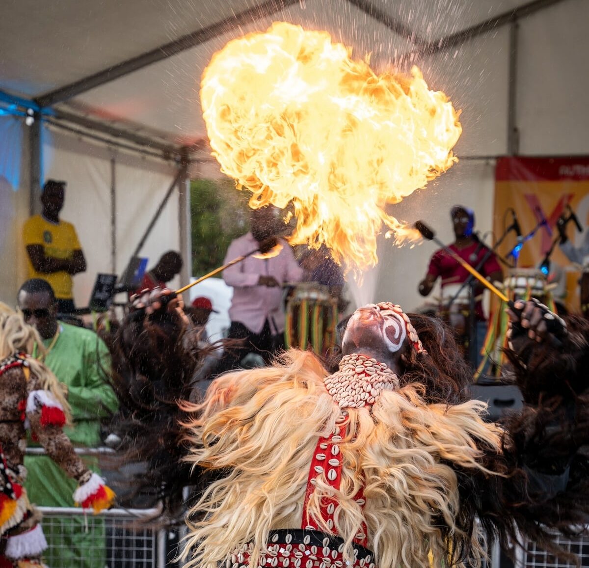 A performer in traditional ornate African clothing spits fire from his mouth.