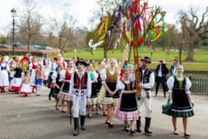 Performers dressed in traditional Slovak costumes march with a wooden pole covered in colorful bunting.