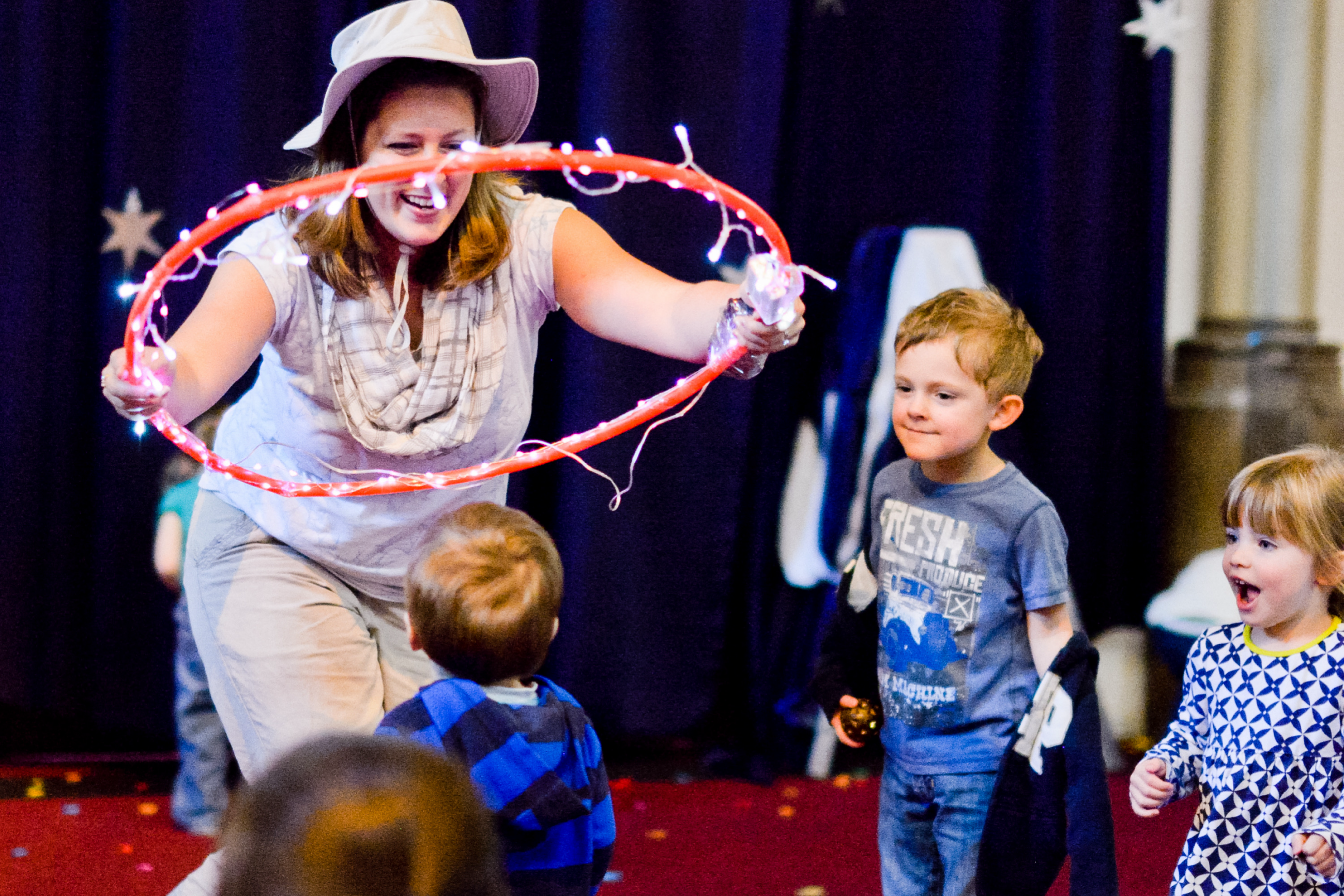 A smiling performance member in costume places a hula hoop with string lights on a young child.