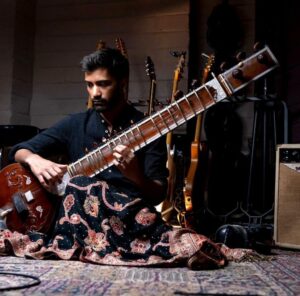 Akash Parekar plays the sitar in a decorated room.
