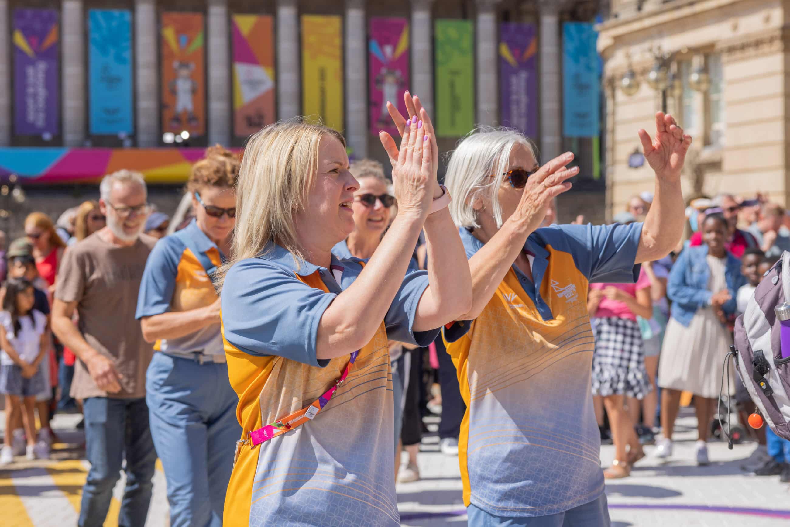 Two volunteers in orange and blue uniforms dance in Victoria Square during the Birmingham 2022 Commonwealth Games.