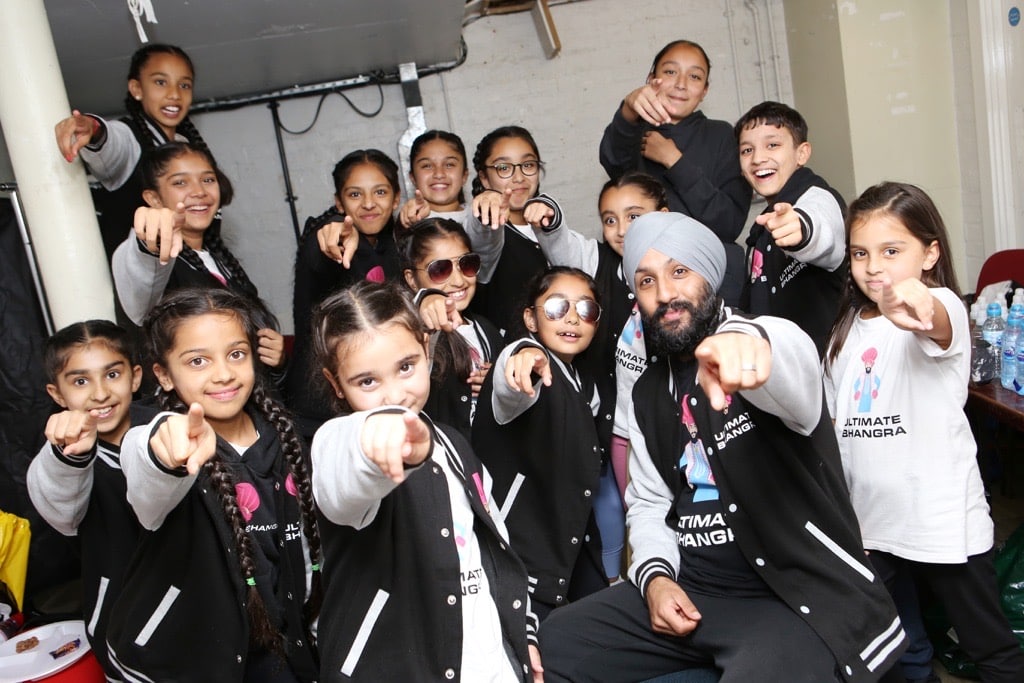 Performer and a team of young people dressed in Ultimate Bhangra jackets point to the camera in a cool pose.