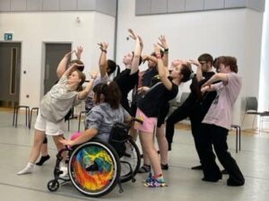 Young dancers, including a member in a wheelchair, practice choreography in a practice room.