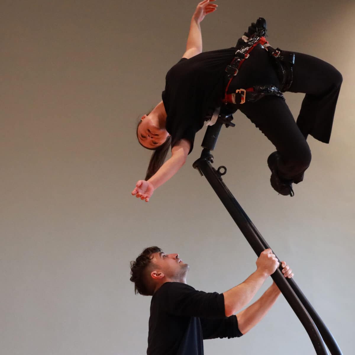 Performer holds a tall counterweighted lift with a performer attached to the top in a weightlessness pose.