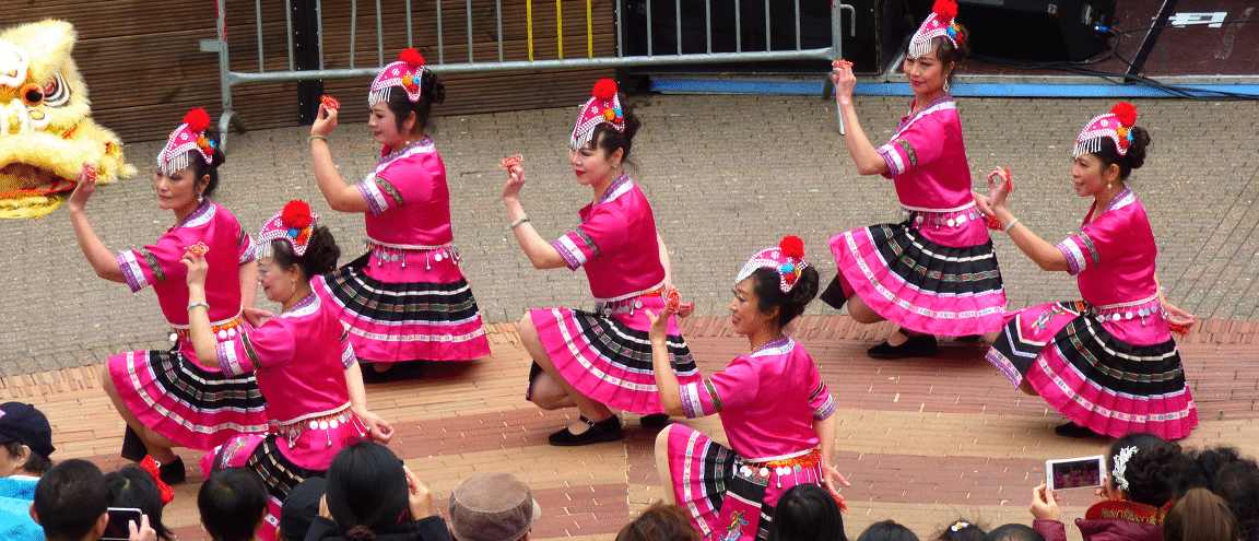 Five dancers in traditional Chinese costumes dance in front of an audience in a street performance.