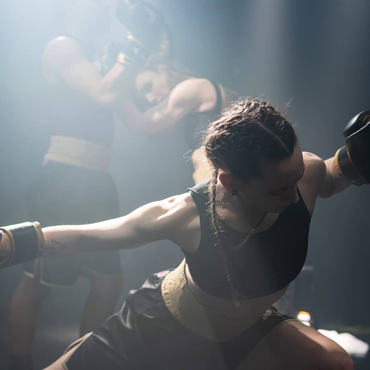 A female young dancer in a performance pose with boxing gloves in dim, dramatic light.