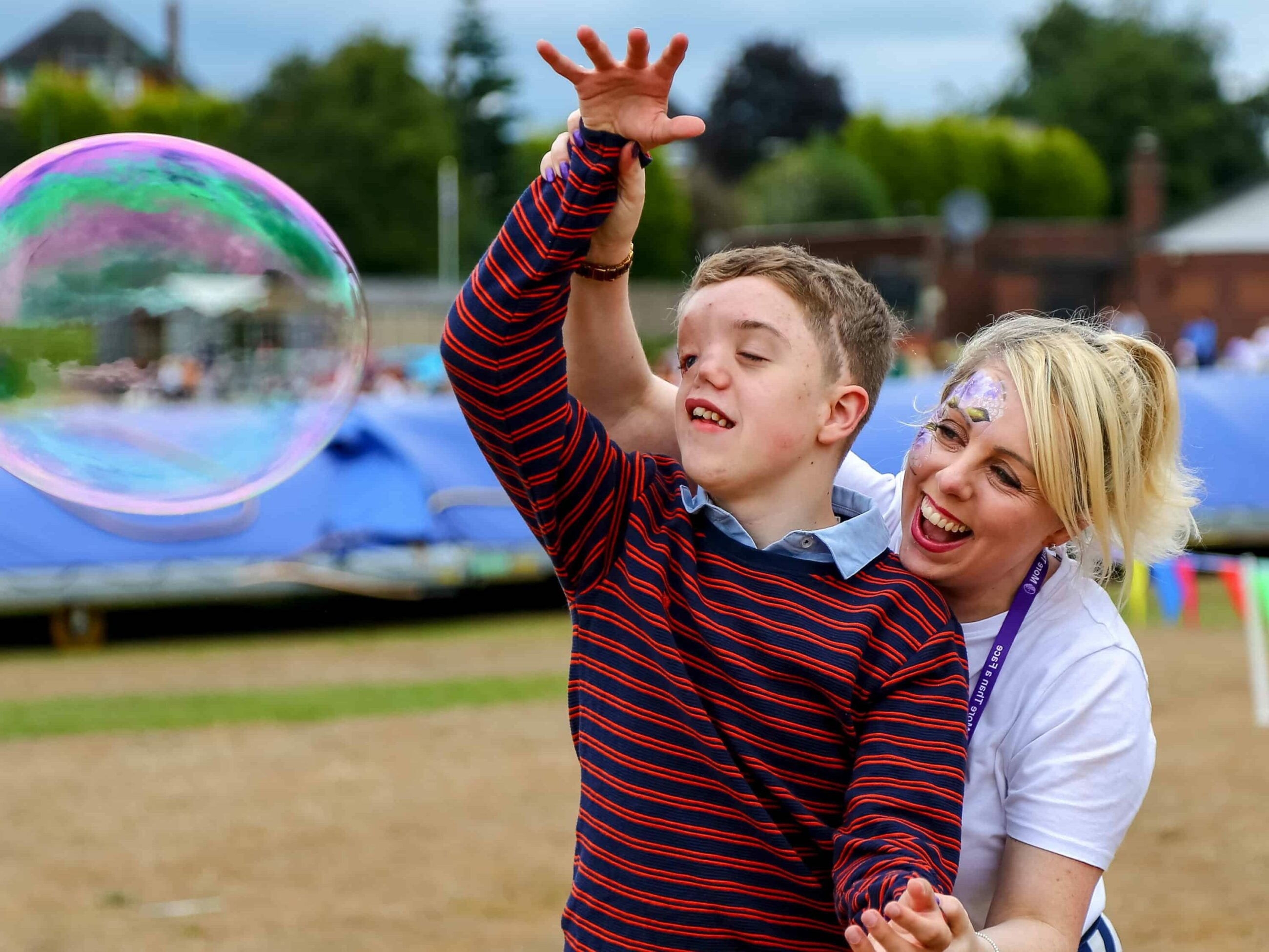 Young child and instructor play with a massive soap bubble in a park.