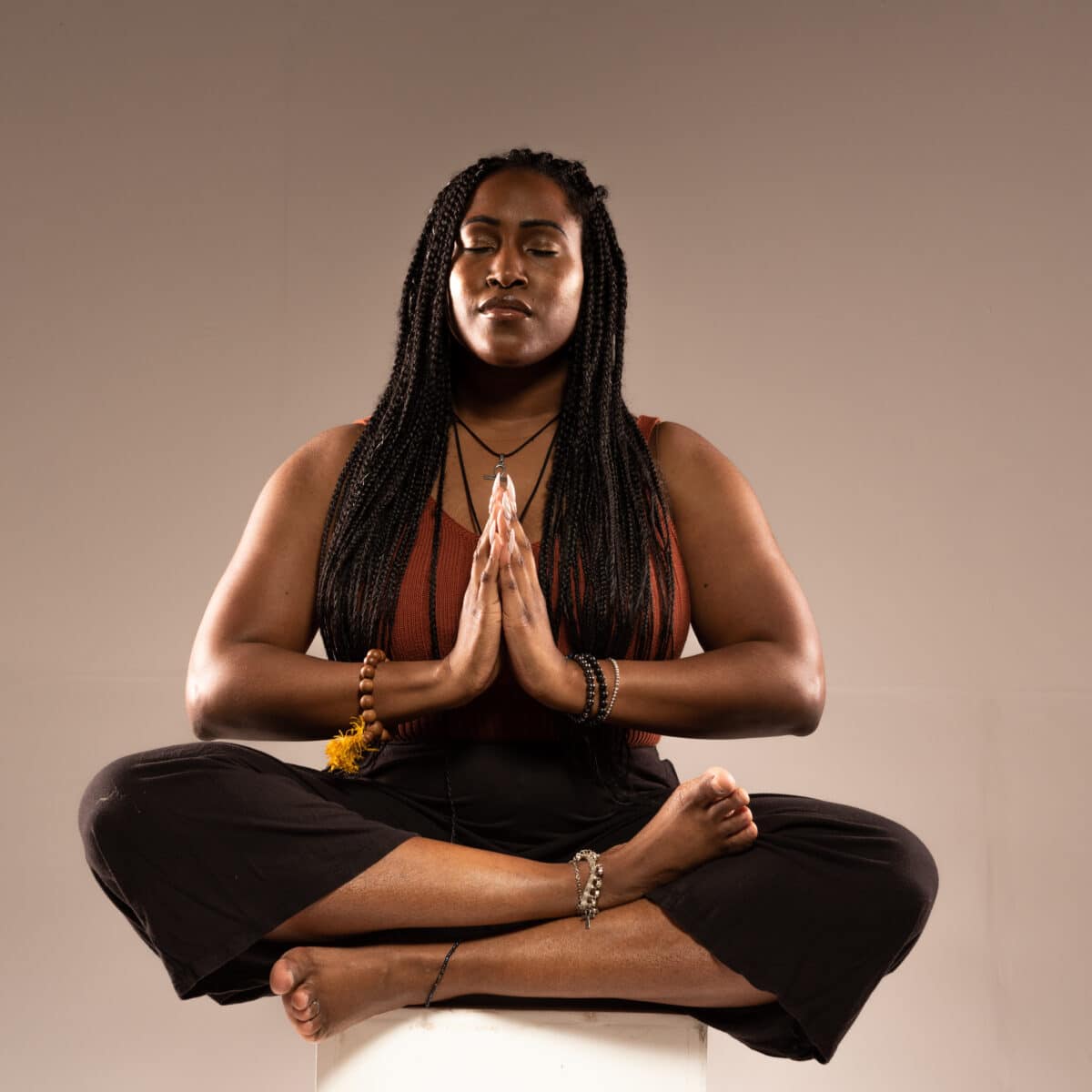 Woman sat in a meditative pose with legs cross, hands pressed together and eyes closed.