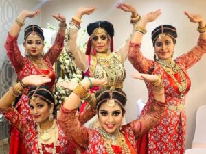 Dancers in traditional costumes pose to the camera in a Bollywood-like pose.
