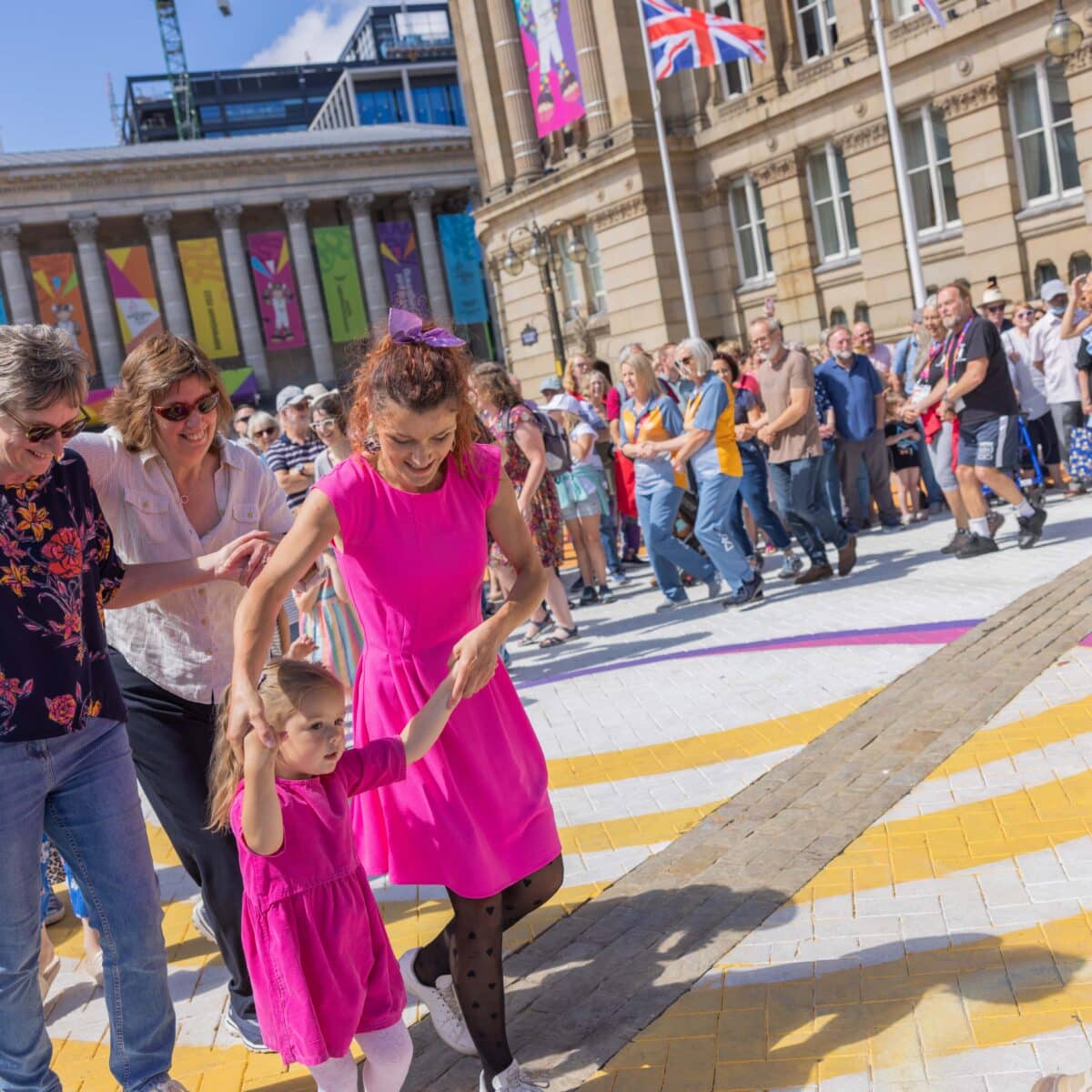 A group of people line dance in pairs in Victoria Square at the Birmingham 2022 Commonwealth Games.