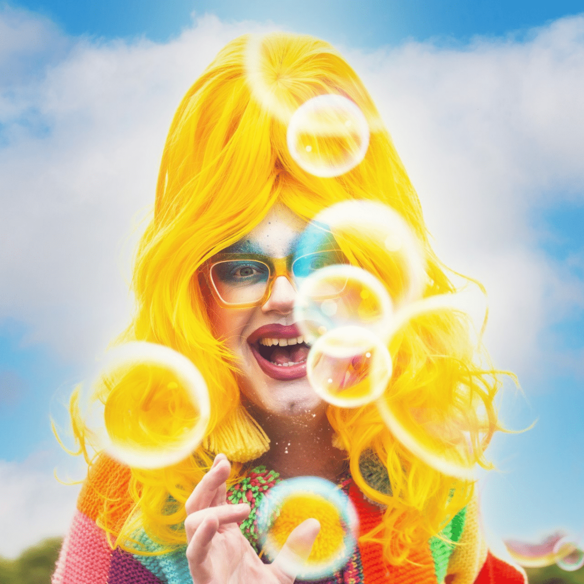Drag performer smiles widely at the camera surrounded by soap bubbles.