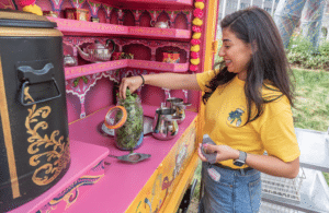 Person makes tea in a traditional-decorated pink moving tea truck.